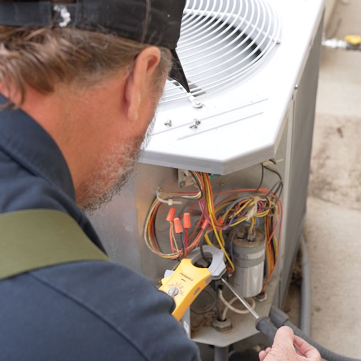 HVAC technician checking wiring and electrical components on outdoor AC unit