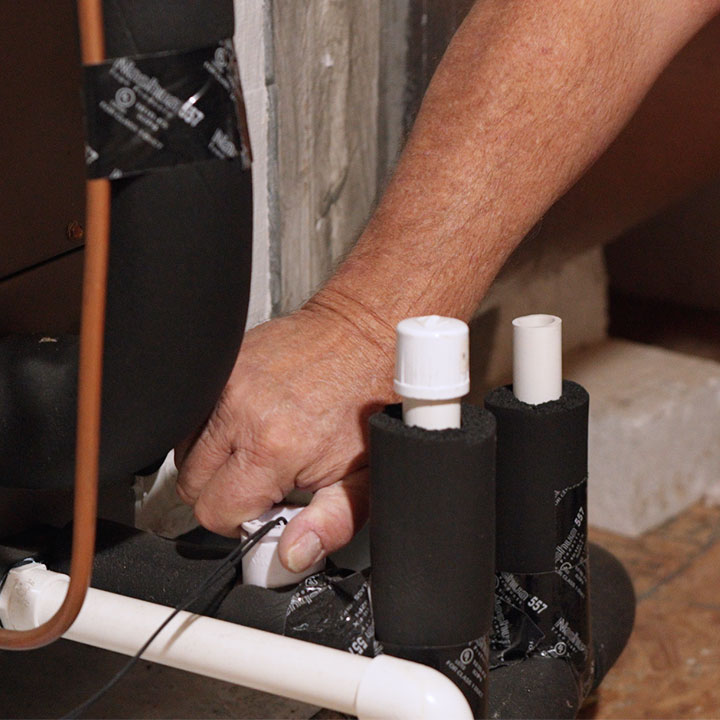 HVAC technician clearing condensate drain line on air conditioning system in attic